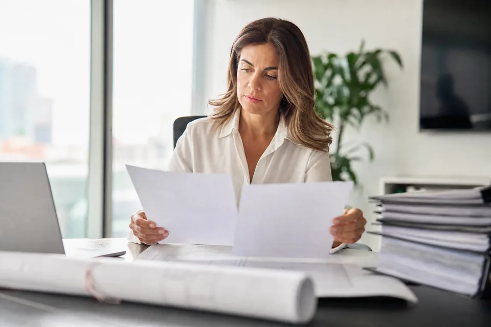 Finance manager holding two printed software quotes side by side at her desk