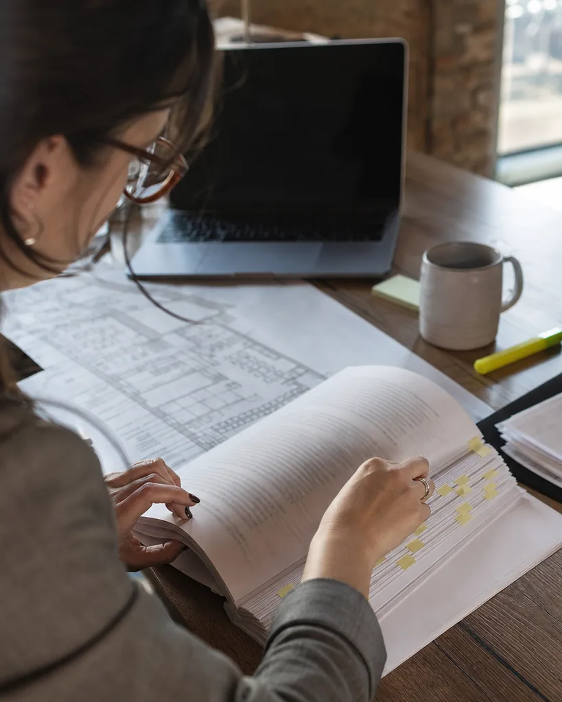Hands flipping through a tabbed commercial store lease next to a printed floor plan on a desk